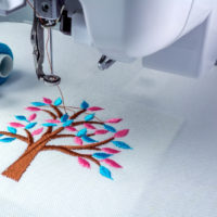 Close up picture workspace of  embroidery machine 
show embroider tree design theme. And two thraed s cyan and pnk color.
